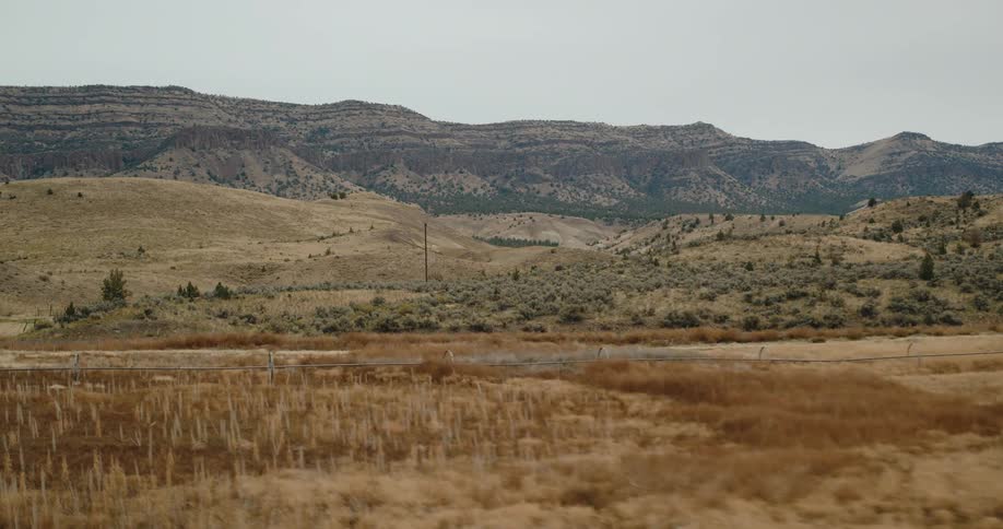 Dry grassy plains stretch out toward layered hills and rugged mountains under a cloudy sky