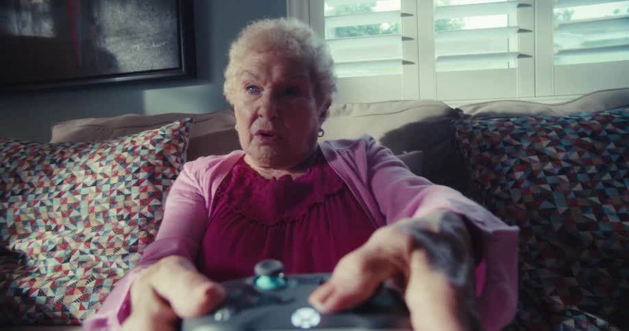 An elderly woman looks focused and surprised while gaming on a couch