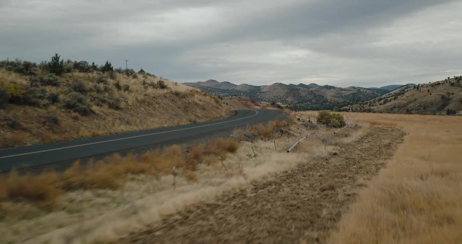 A winding road cuts through a dry hilly landscape under an overcast sky