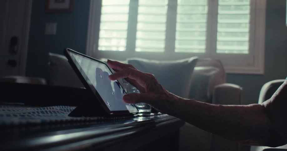 An elderly person uses a tablet at home in a softly lit living room