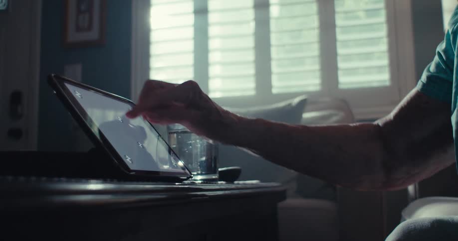 An elderly person uses a tablet in a sunlit cozy living room