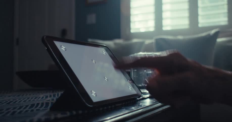 An elderly persons finger touching the screen of a tablet that is resting on a table
