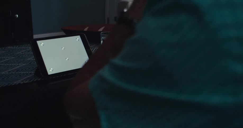 The hand of a person wearing a blue shirt who is looking at a tablet that is on a table with a white screen and the person is making hand gestures