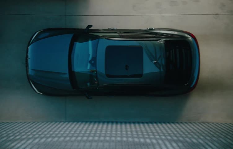 Aerial view of a black vehicle driving out of a large curved metallic structure