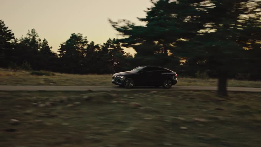 Aerial of a car driven on a road in the middle of a woodland area at sunset
