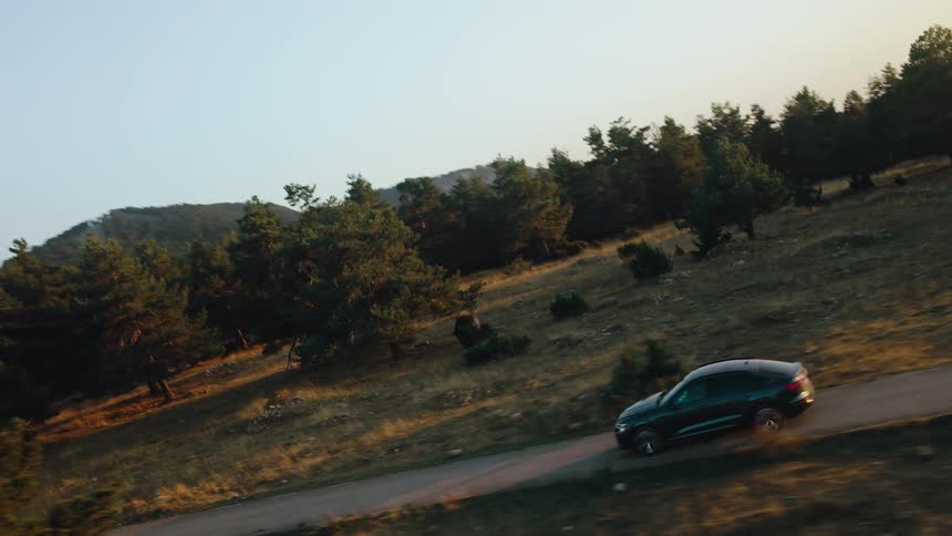 Aerial of a black sedan driving along a rural road in an evergreen forest