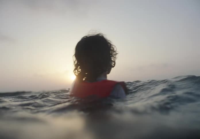 The child is swimming in the ocean with a life vest