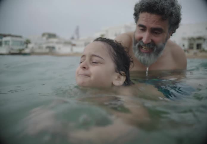 Grandfather teaches his grandson how to swim in the waters off a coastal town on a summer day