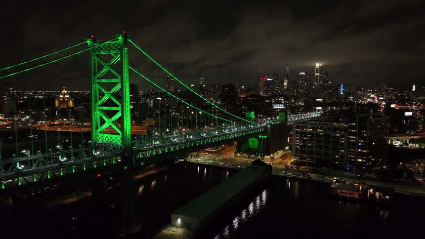 A Benjamin Franklin Bridge in Philadelphia is lit up green at night