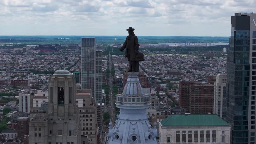 An aerial view shows Philadelphia City Hall and William Penn statue with the expansive cityscape stretching out behind it under a cloudy sky