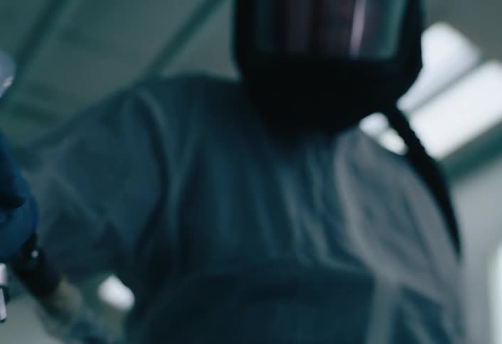 A person in full protective gear and respirator holds a spray nozzle in a sterile environment