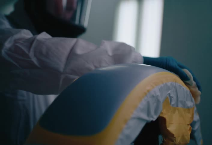 Person wearing a helmet and gloves holding a sponge and wiping it on a plastic surface