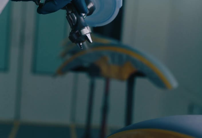 A person wearing gloves spray paints objects masked with tape on a clean workshop