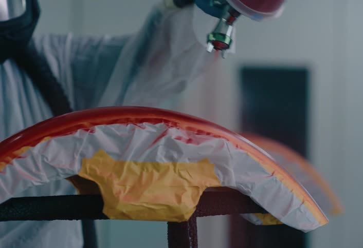 The worker is spraying paint on the object