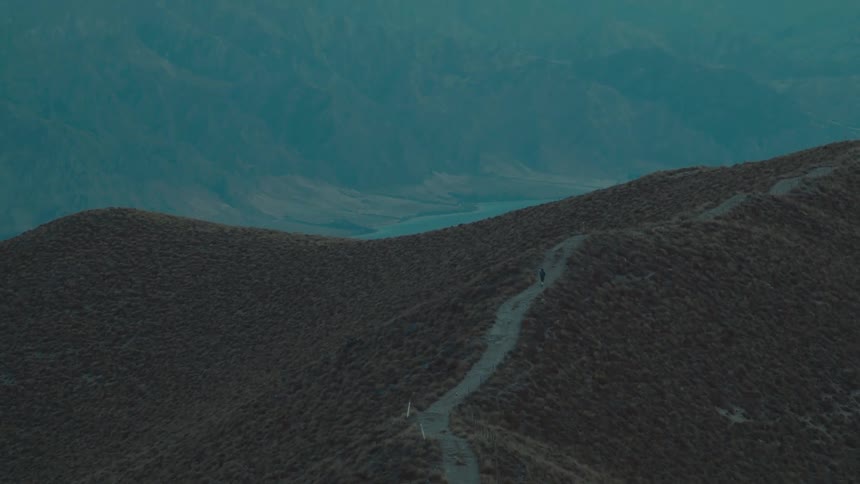 Person walks along a dirt path near a foggy valley after dusk