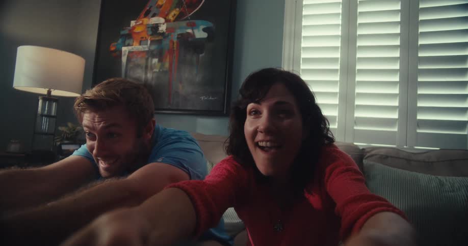 Woman and man laugh while energetically playing a video game at home during the daytime