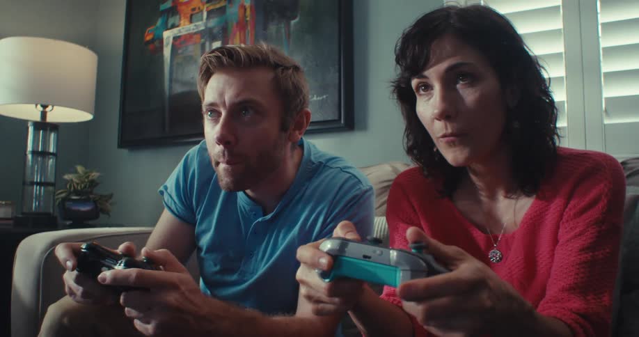 A man points towards the television while playing video games with a woman