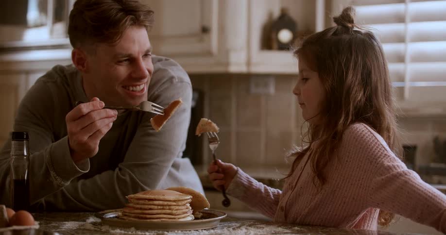 A father and daughter eat pancakes together at home