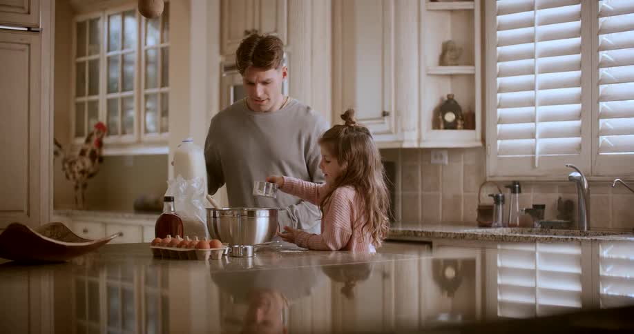 A father pours milk into a cup so his daughter could add it to a bowl