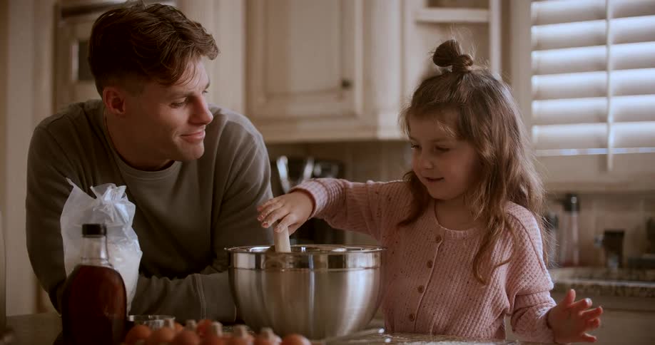 A father watches his daughter mix food in a bowl