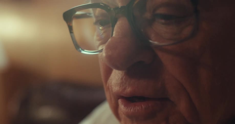 In a warm dimly lit room an elderly person with glasses intently marks a nursing reference guide with a pen