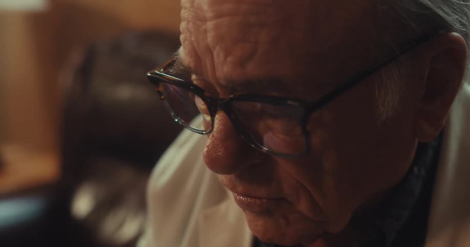 Elderly man with glasses and white coat sitting and talking