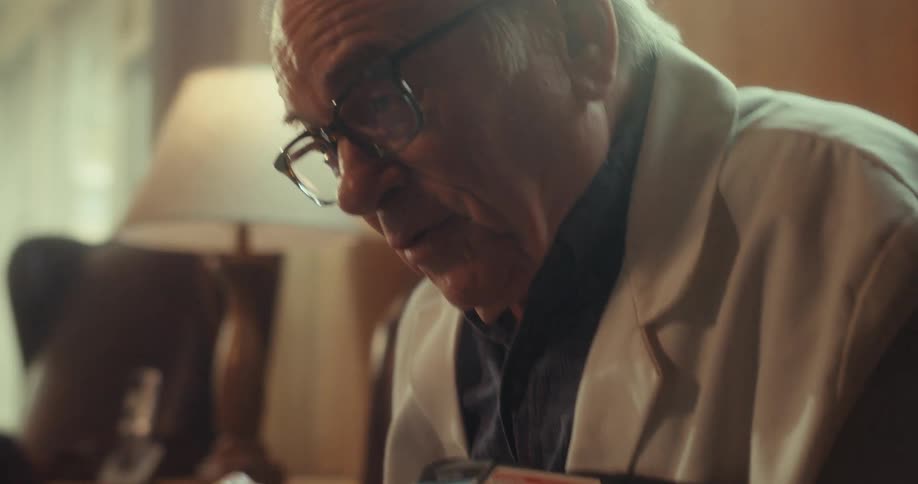 Elderly man sitting holding a device and giving a presentation