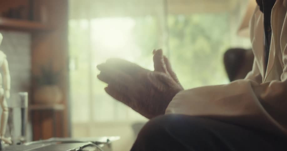 Close up of elderly doctors hands pressed together as he demonstrates while in an online consultation in living room