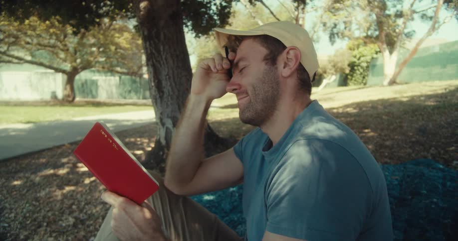 Man lays down on a lawn after reading while sitting outdoors in the middle of the day