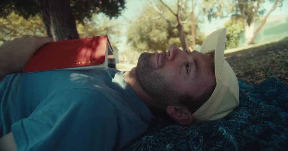 Young man journals and a rests while laying down outdoors under a tree during daytime