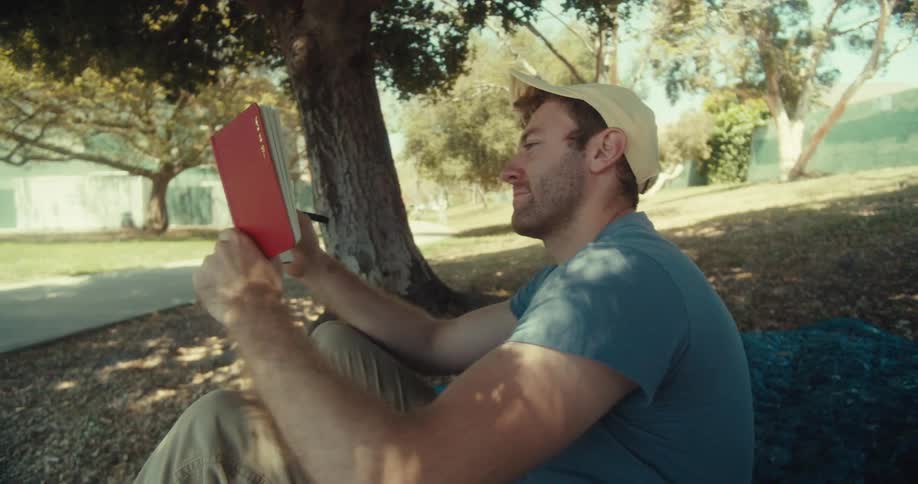 Man lays down on a lawn after journaling while sitting outdoors under a tree during daytime
