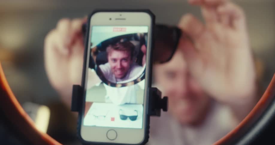 Young man shoots and records media content about sunglasses with an iphone and ring light while sitting in a living room