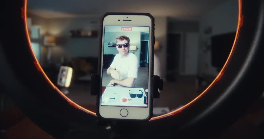 Young man shoots and records media content with an iphone and ring light while sitting in a living room