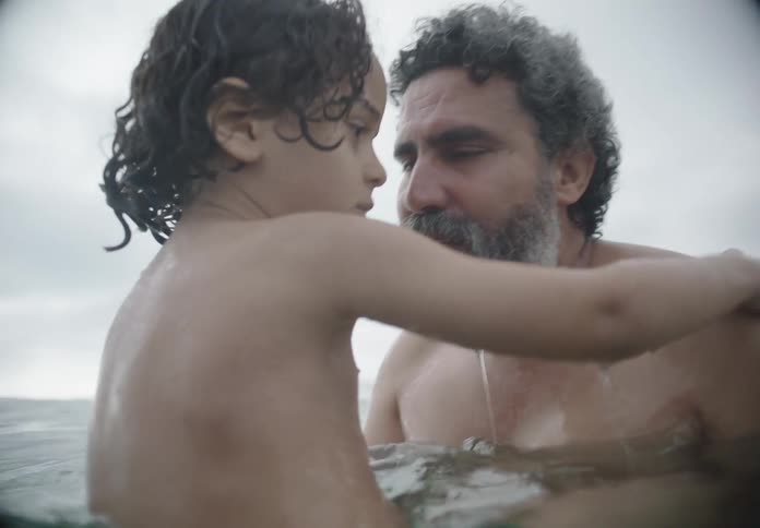 A father is holding his son and talking to him in the ocean