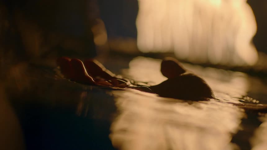 A hand floats in water as flames reflect on the surface