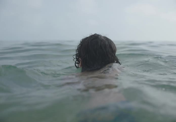 The boy is swimming in the water on a cloudy day
