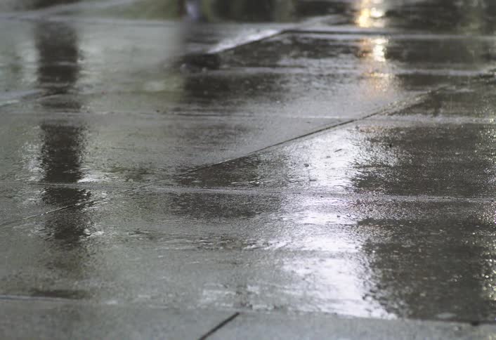 Rain falling on a city sidewalk with people walking in the background