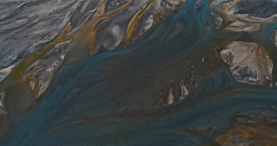 Abstract vein like patterns of a glacial river delta with turquoise water flowing through black volcanic sand and golden sediment deposits