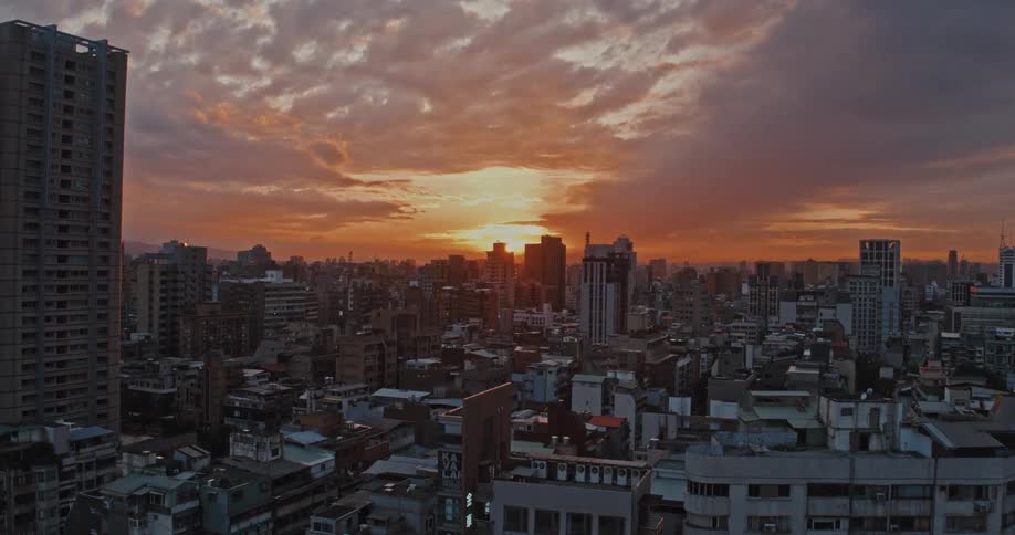 A vibrant sunset casts warm light over a dense city skyline filled with highrise buildings