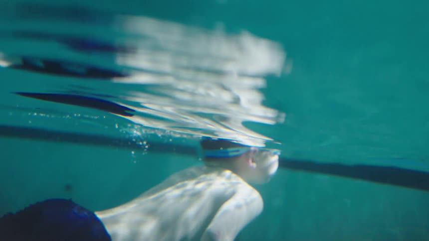 A kid swims in a pool at midday