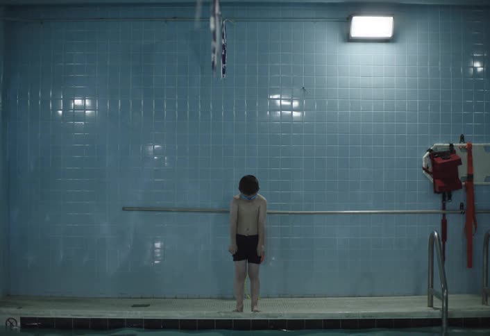 Boy child standing at the edge takes a dive into the indoor pool