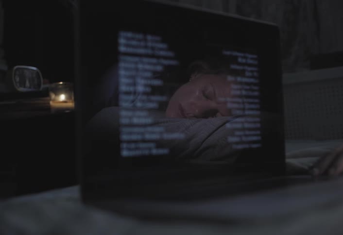 Close up of a laptop screen at night showing post movie credits and the reflection of a woman sleeping on bed