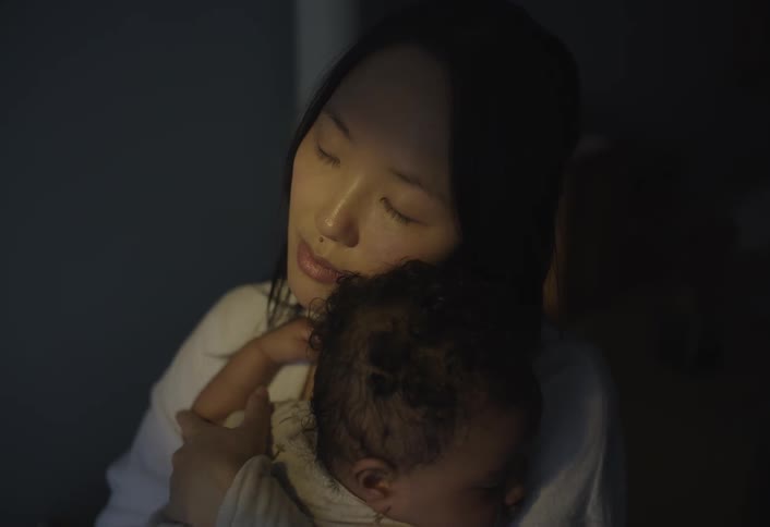A mother gently holds her sleeping baby in a dimly lit room