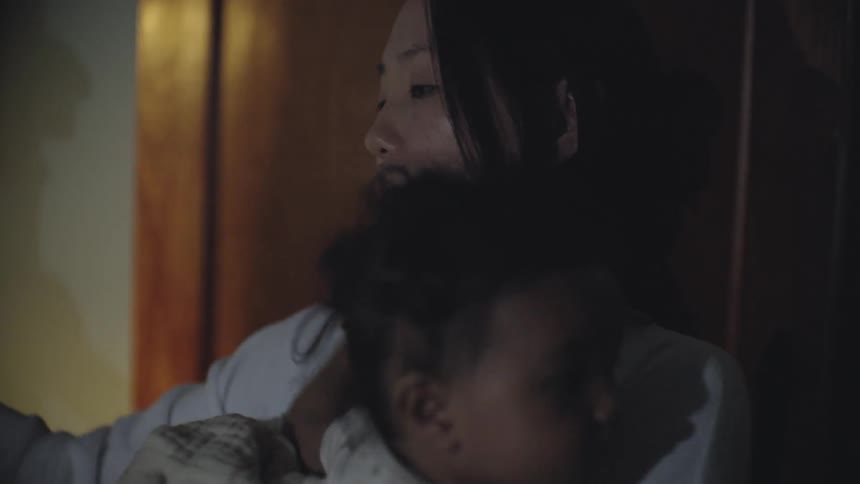 A young woman holding an baby puts an item back into a refrigerator and closes its door
