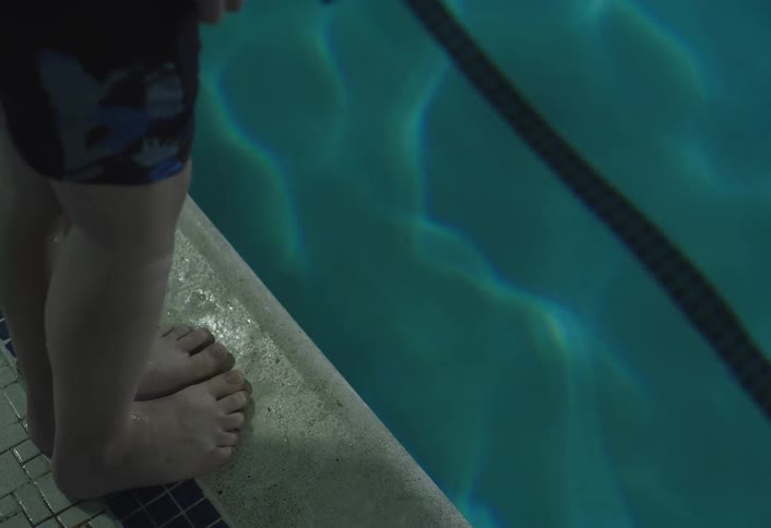 Close up of a boys leg as he stands at the pools edge and jumps into the pool shortly after
