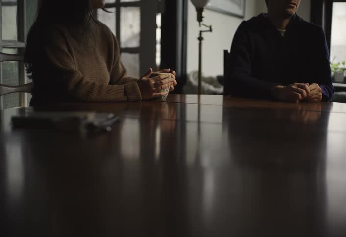 Two people sit across from each other at a dimly lit table engaged in a quiet conversation