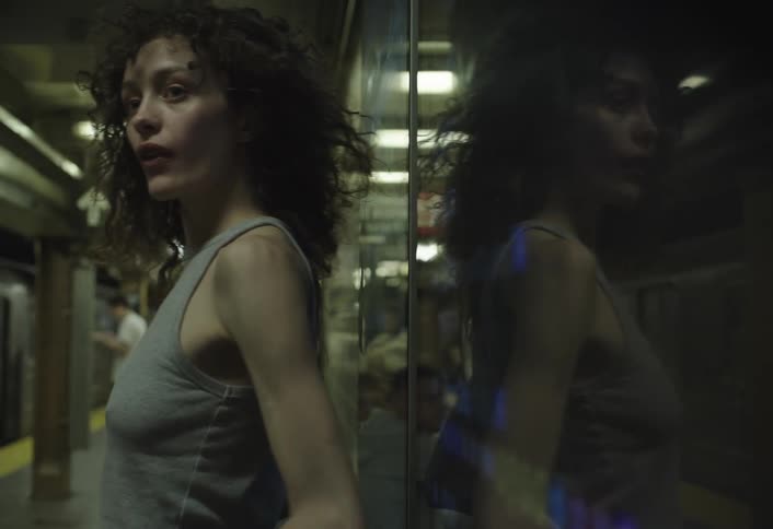 Restless woman leaning against a subway wall with a stream of other people walking by