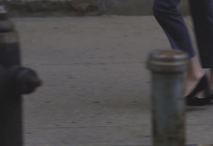 A woman in high heels and pants walking quickly on a city sidewalk