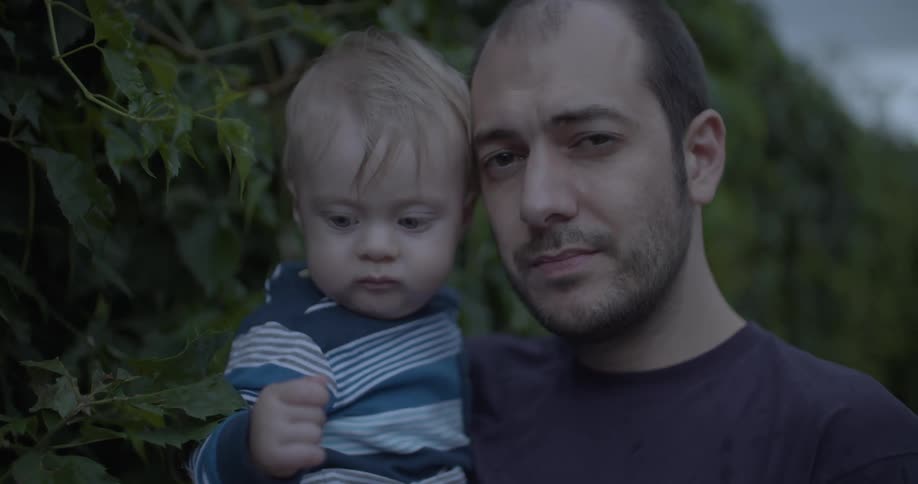 Close up portrait of father and son standing outdoors in front of a plant fence during daytime