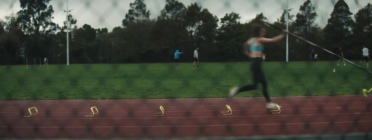 Female pole vault athlete runs past as she practices pole planting on a track outdoors during the day